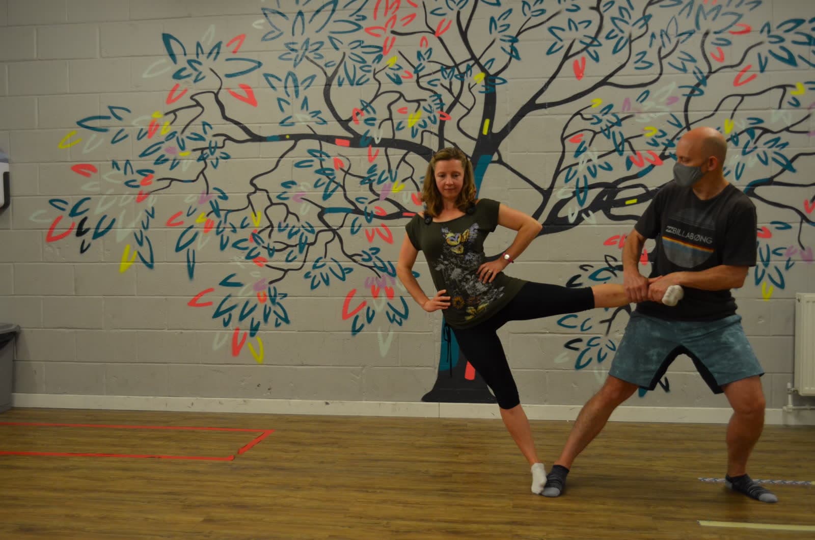 A coach holding a climber’s raised leg through a hip stretch in the studio