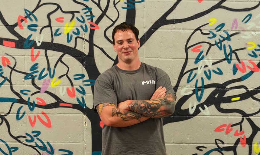 A coach in front of the painted tree mural in the studio, arms folded