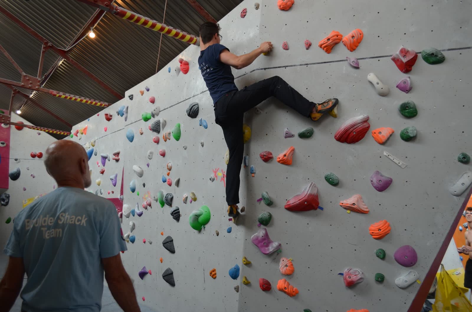 A climber working a problem while a coach watches from below