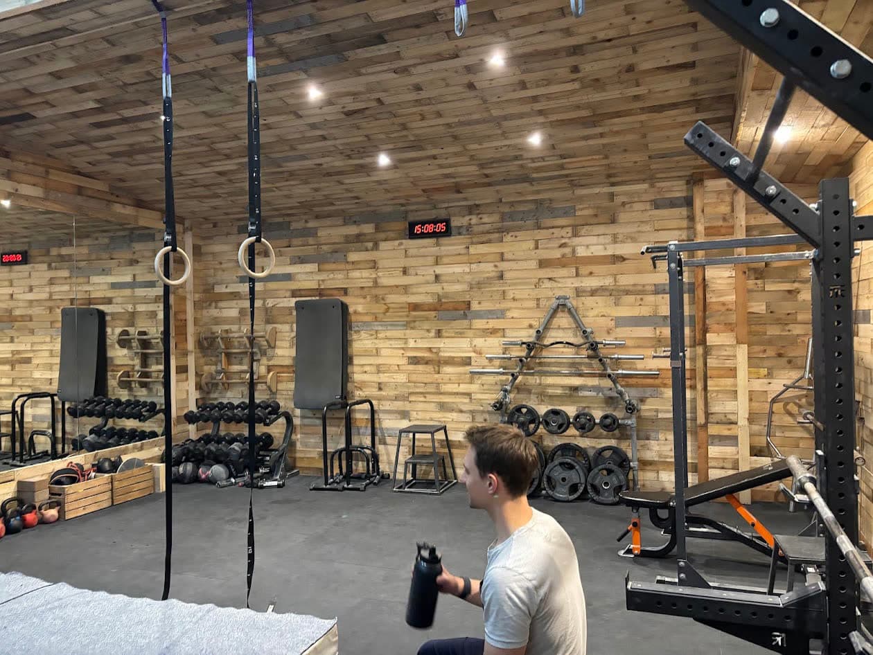 Rings and straps hanging in the pallet-walled training area, racks and weights behind