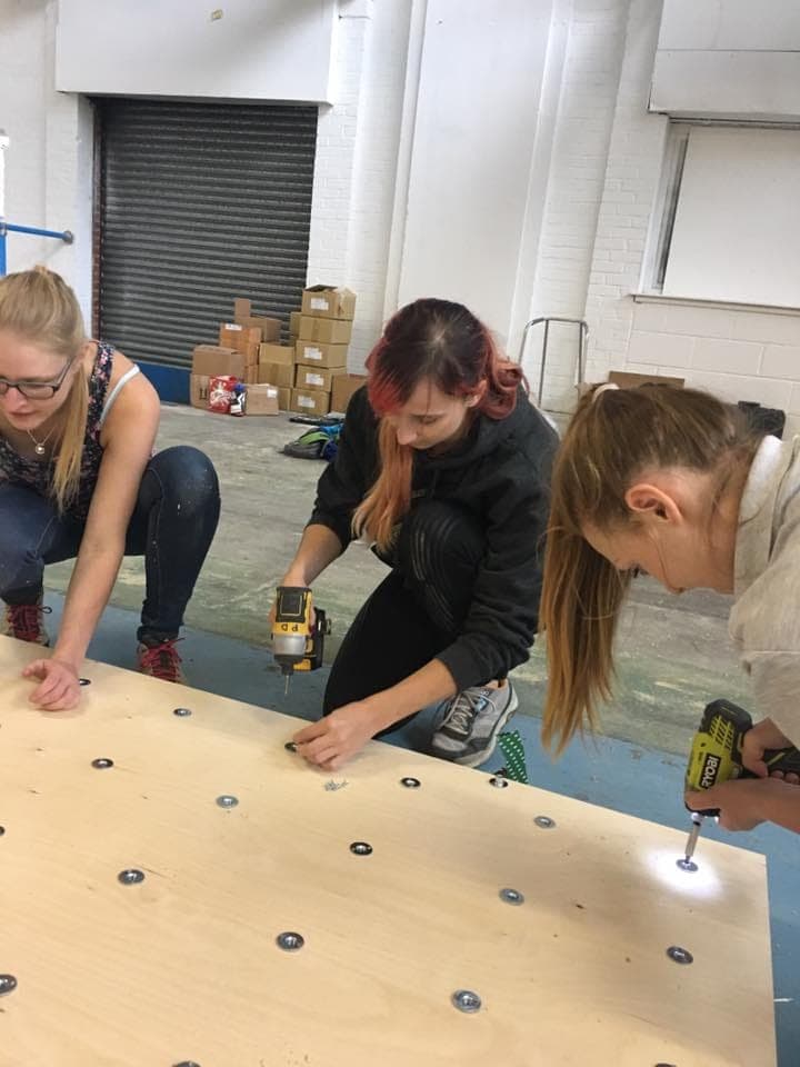 Three volunteers kneeling on a sheet of plywood, fitting T-nuts