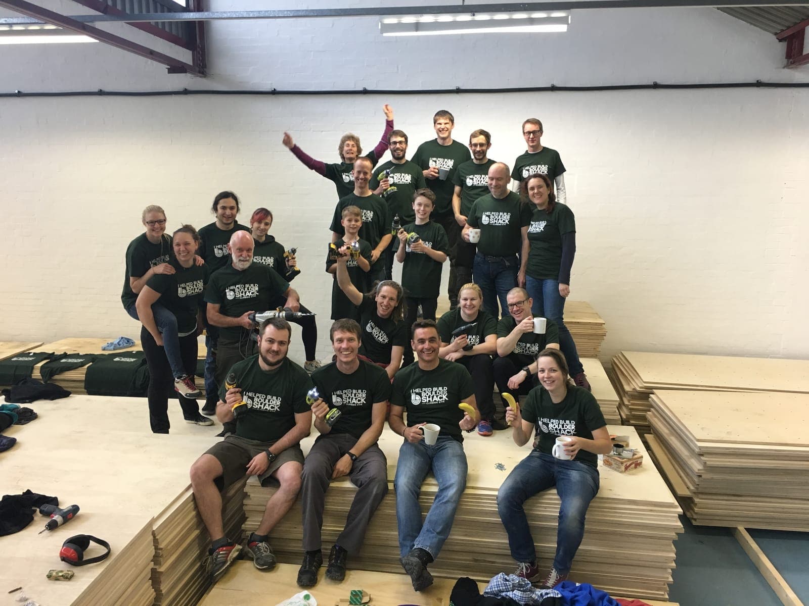 Volunteers in green I Helped Build Boulder Shack T-shirts, sat on stacks of plywood with drills and mugs