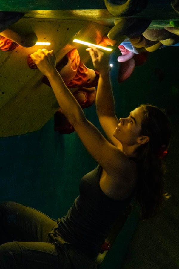 A competitor reaching up through the cave under coloured lights