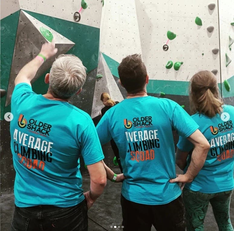 Three climbers in Older Shack T-shirts looking up at a problem