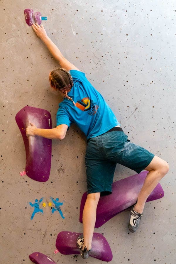 A young climber in a Boulder Shack T-shirt mid move at the Youth Climbing Series