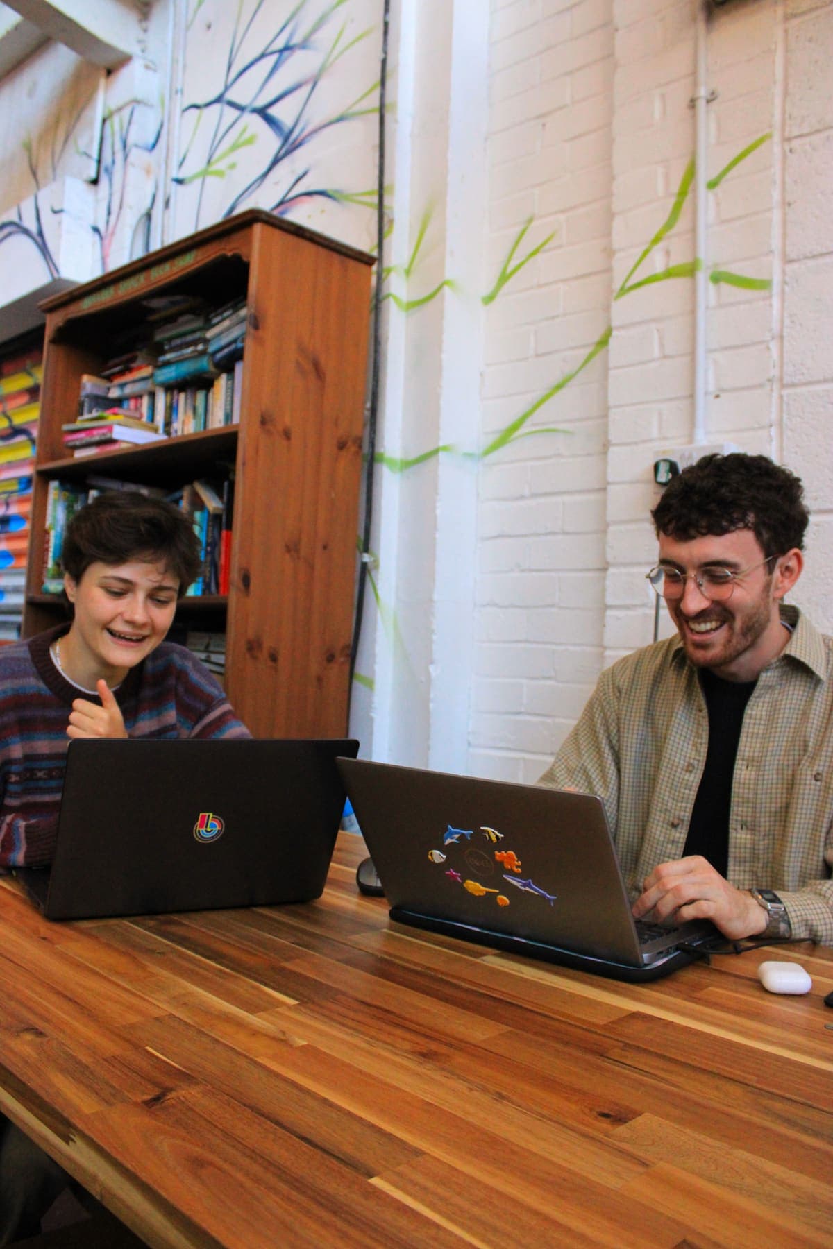 Two people laughing over their laptops at a café table