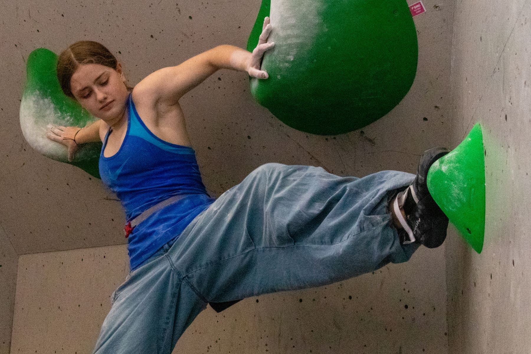 A climber leaning out from a big green hold
