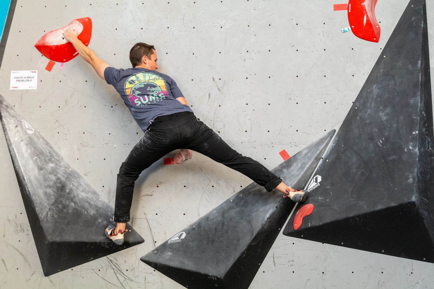 A climber stretched between two black volumes at a competition