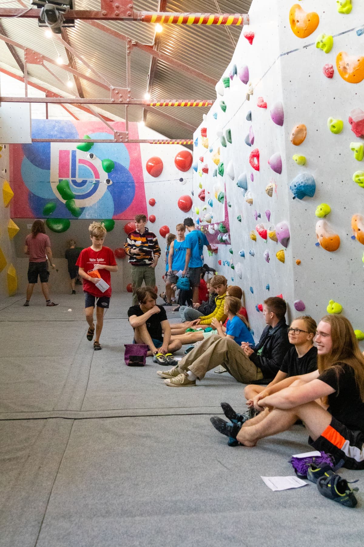 Young climbers sitting along the mats under the bunting, waiting for their turn