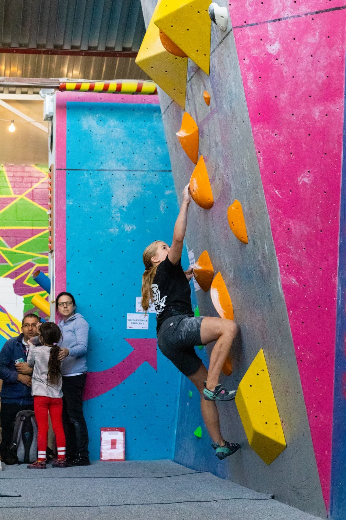 A young climber on the wall with others watching from below