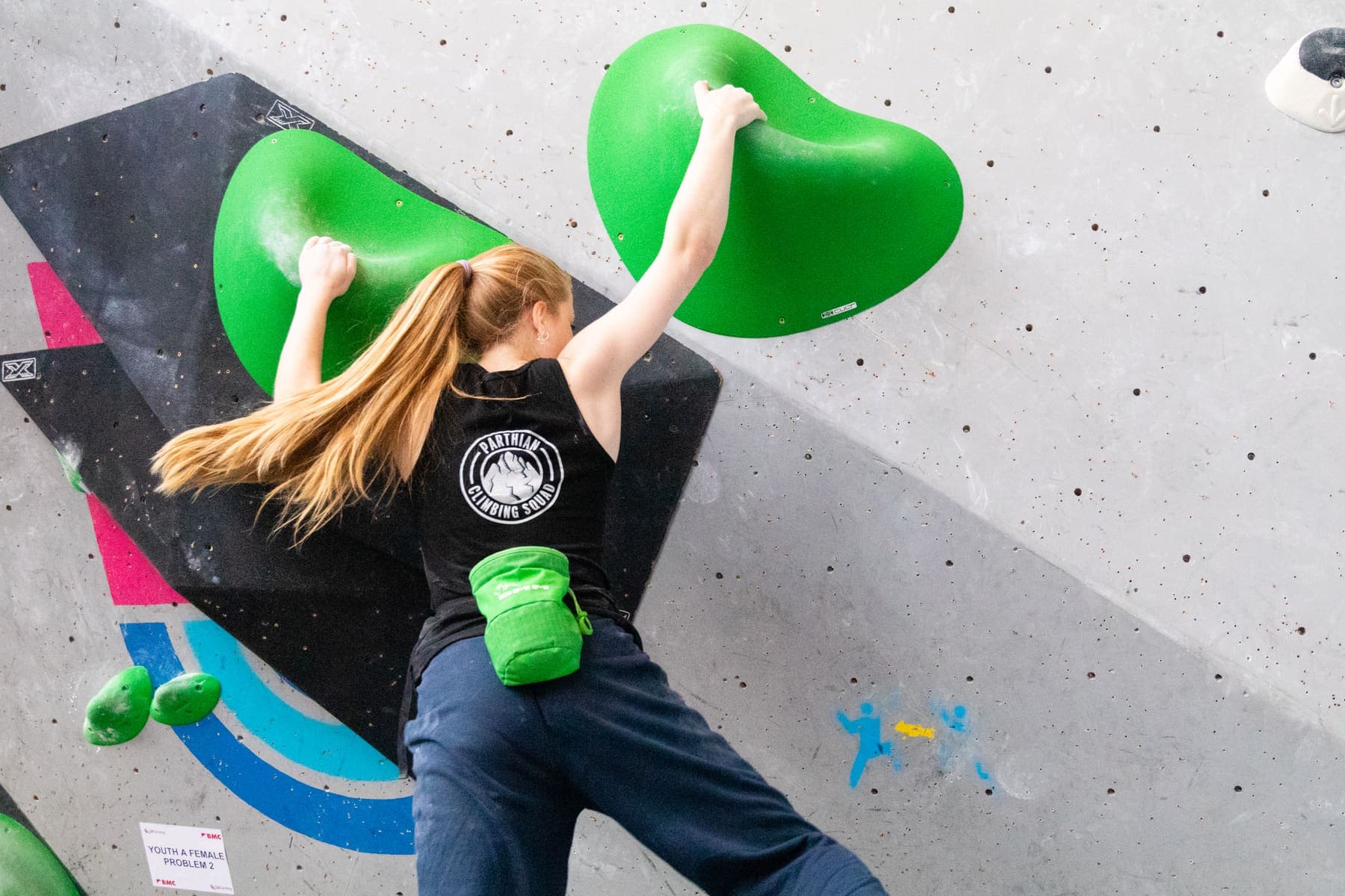 A teenage climber holding two big green holds on a steep wall