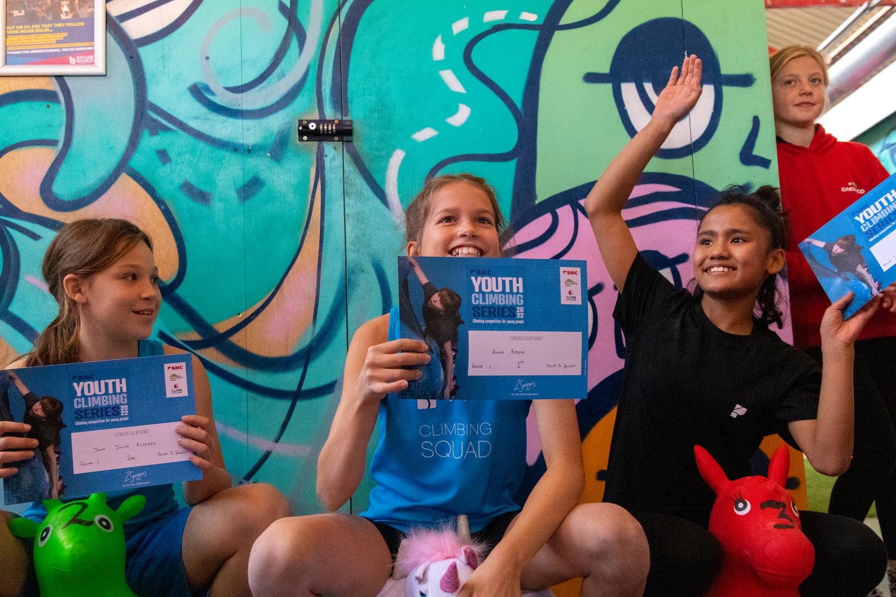 Young climbers cheering with their certificates in front of a mural