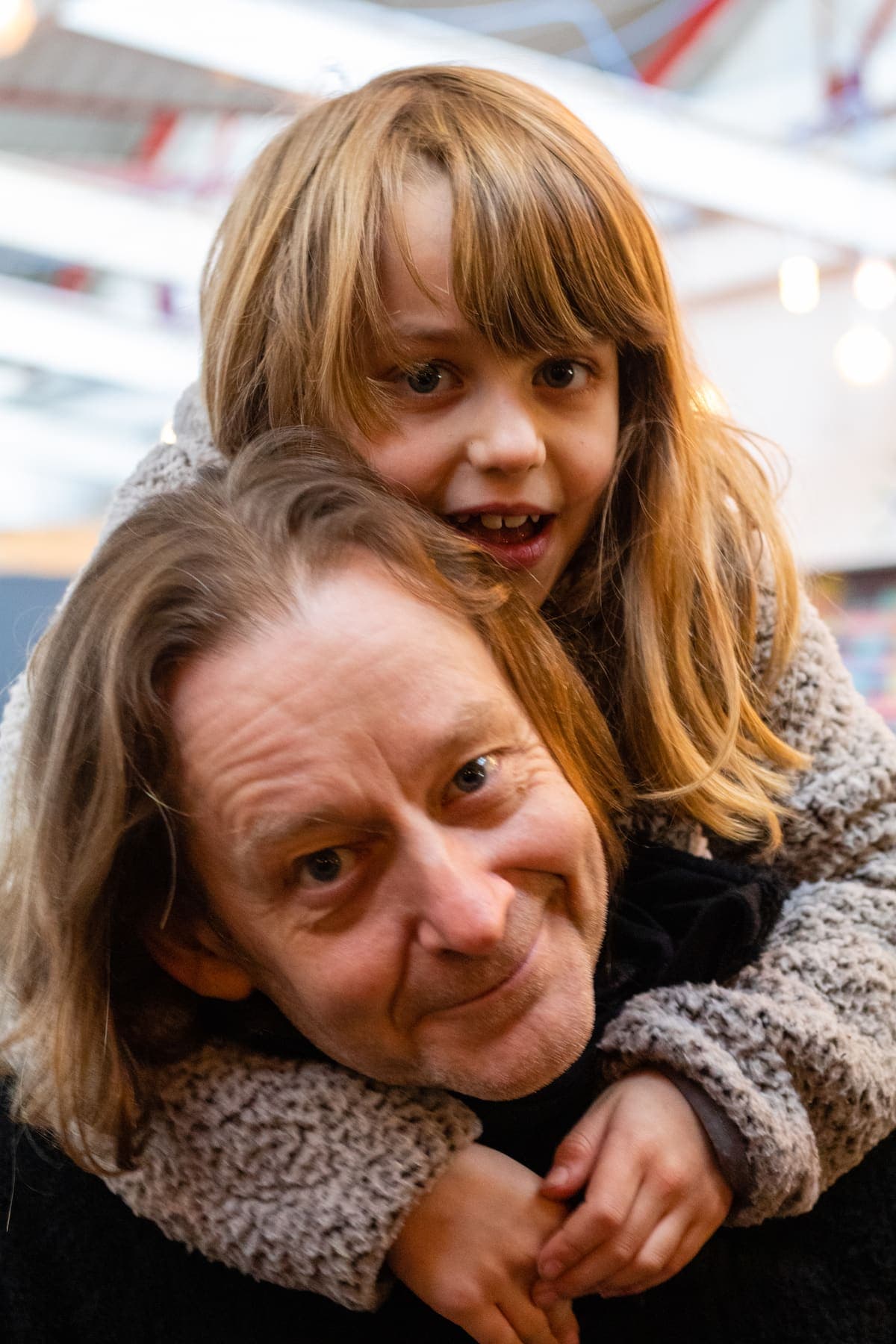 A grown up giving a child a piggyback, both grinning at the camera
