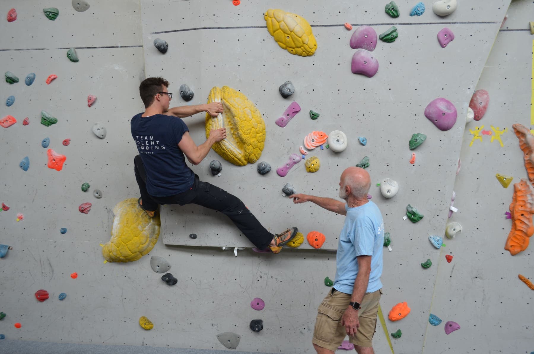 A coach pointing out the next foothold to a climber on the wall