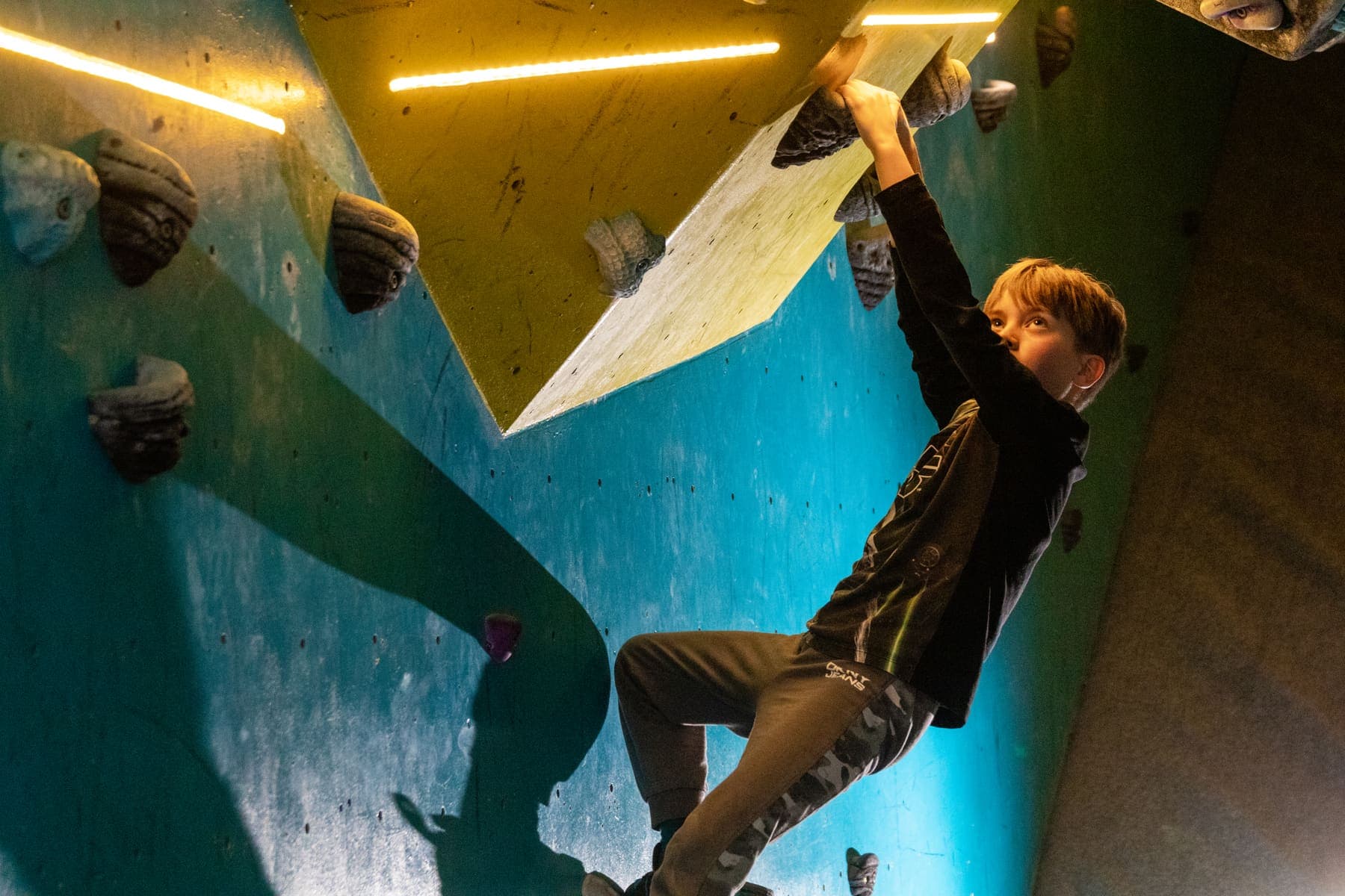 A teenage climber hanging from a steep yellow overhang