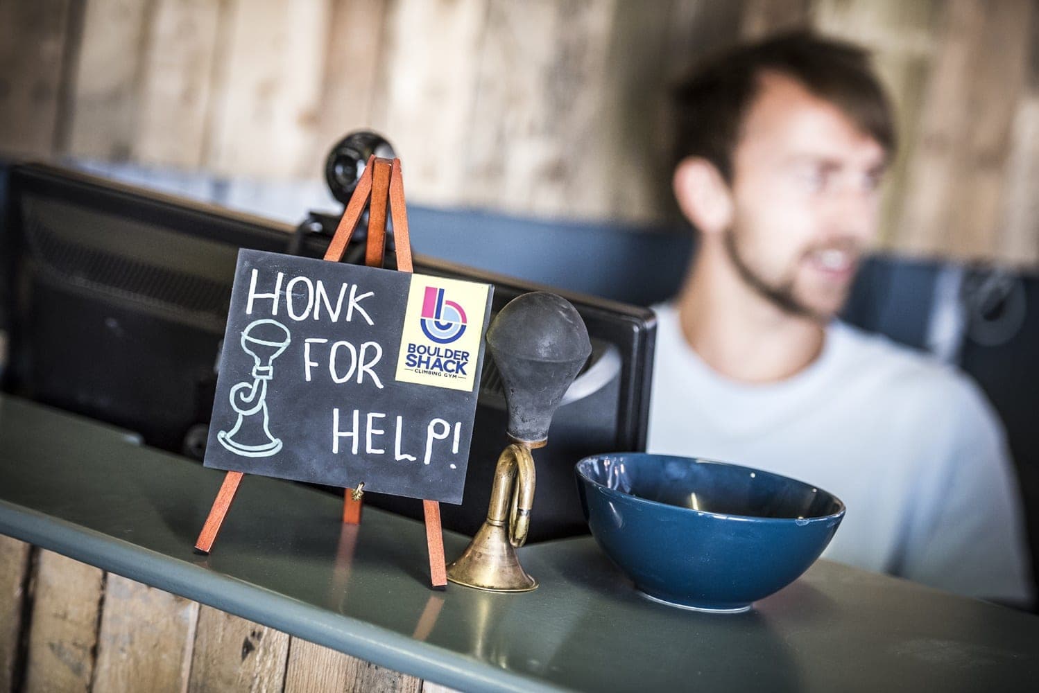 A chalkboard on the front desk saying Honk for help, beside a brass horn, with one of the team smiling behind it