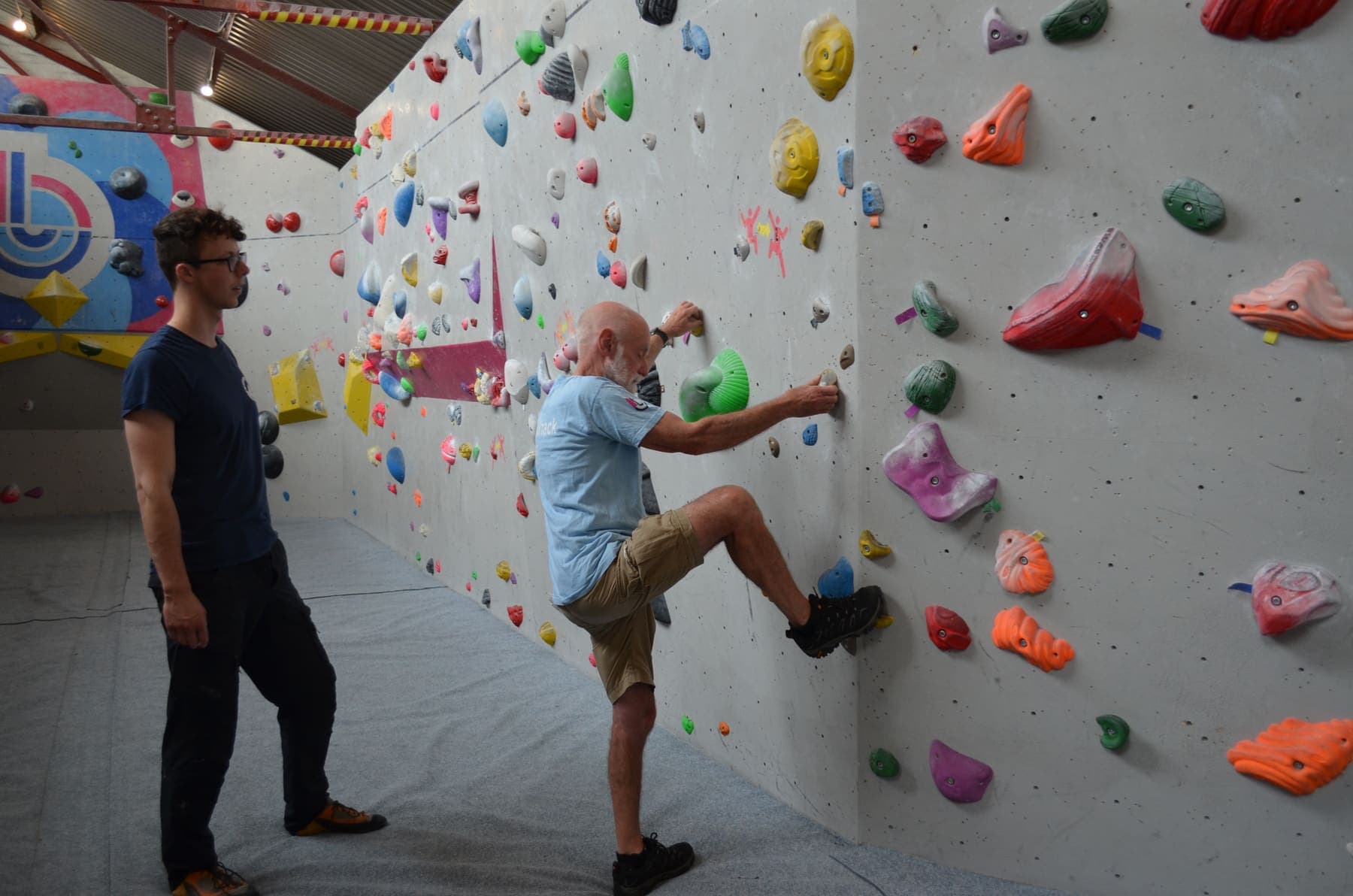 An older climber stepping up onto the wall with an instructor watching