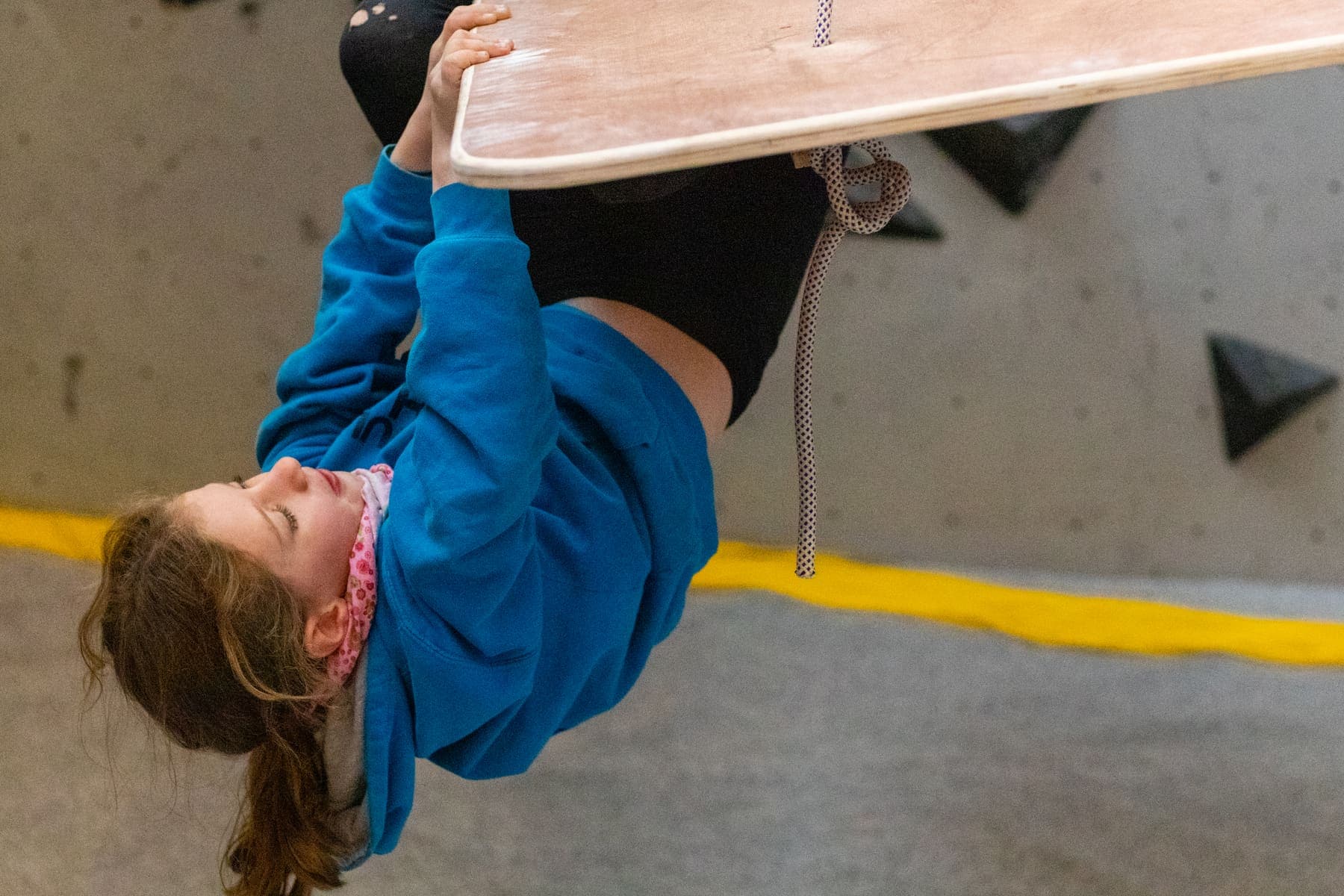A child hanging upside down from a climbing board, laughing