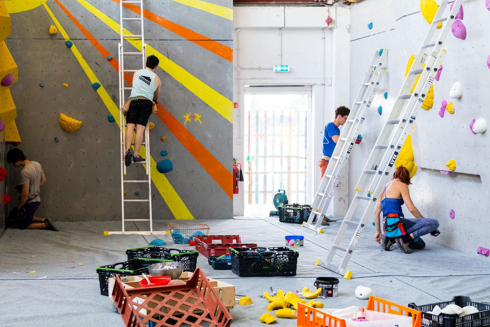 Crates of washed holds on the mats while setters work up ladders on a stripped wall