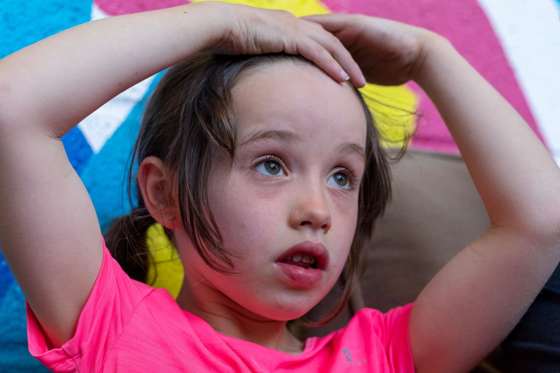 A girl with her hands on her head, looking up at the wall