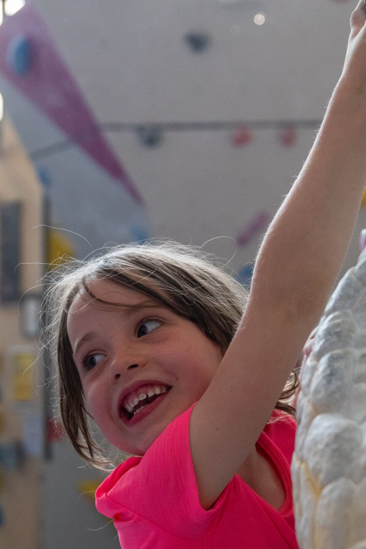 A girl smiling as she stretches up for a hold