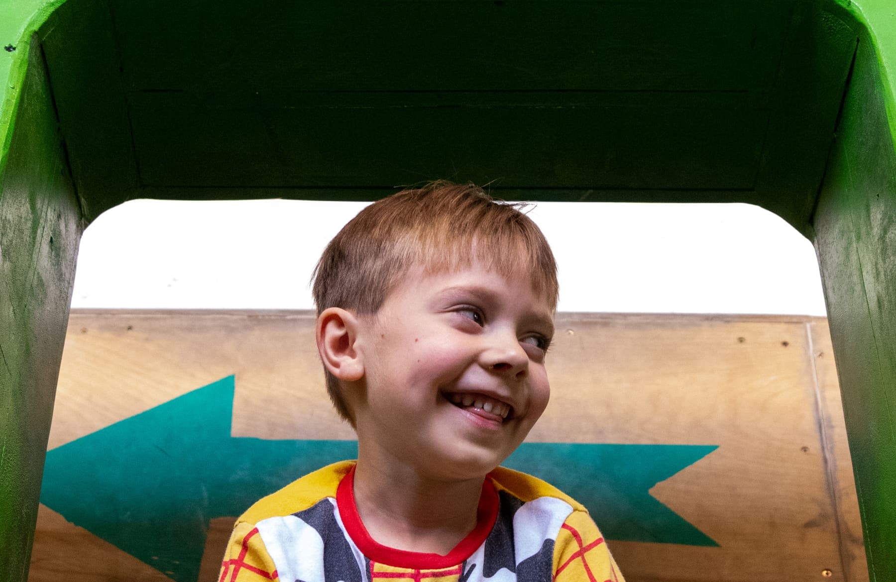 A small boy grinning out of a climbing tunnel