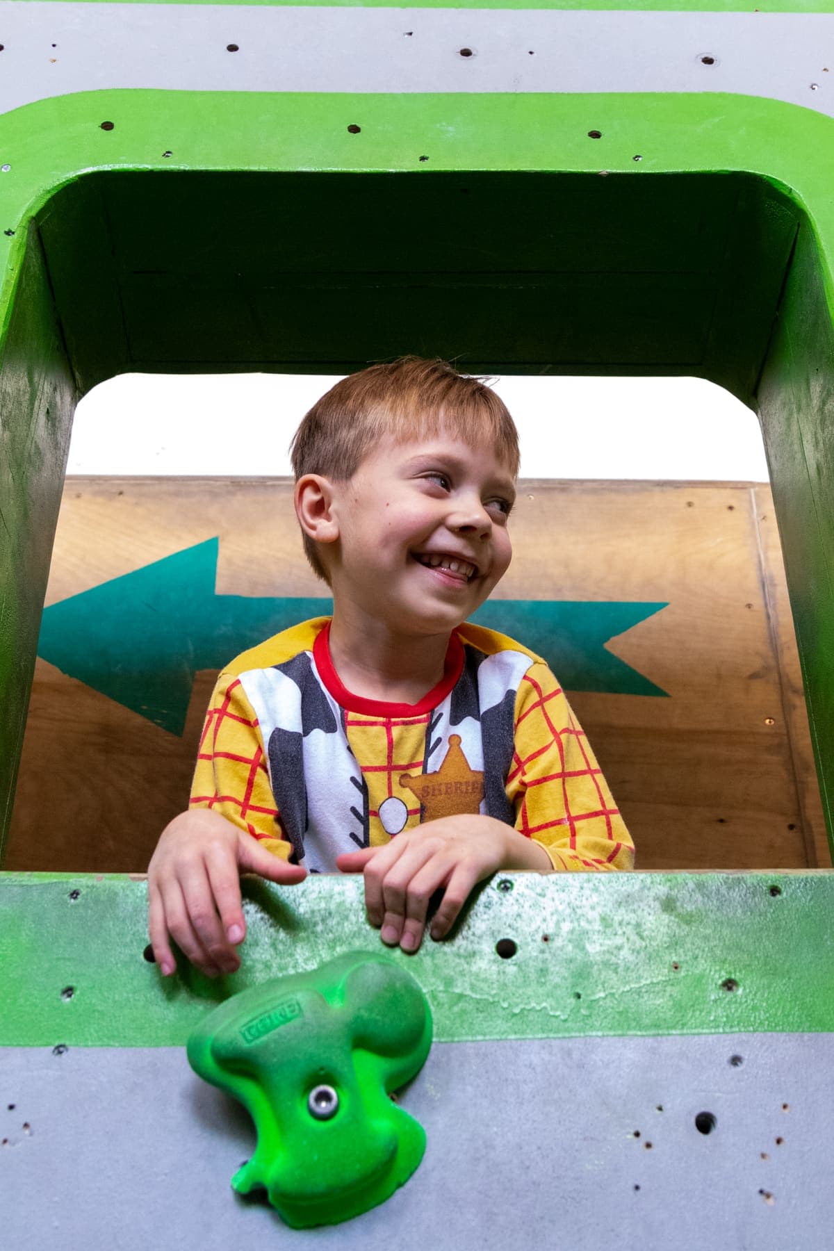 A boy grinning out of a climb-through tunnel in the wall