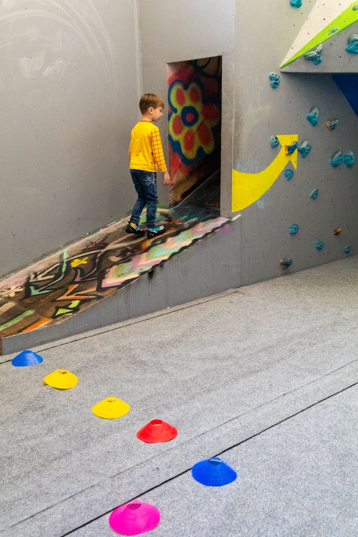 A boy walking up a ramp past a trail of coloured stepping holds