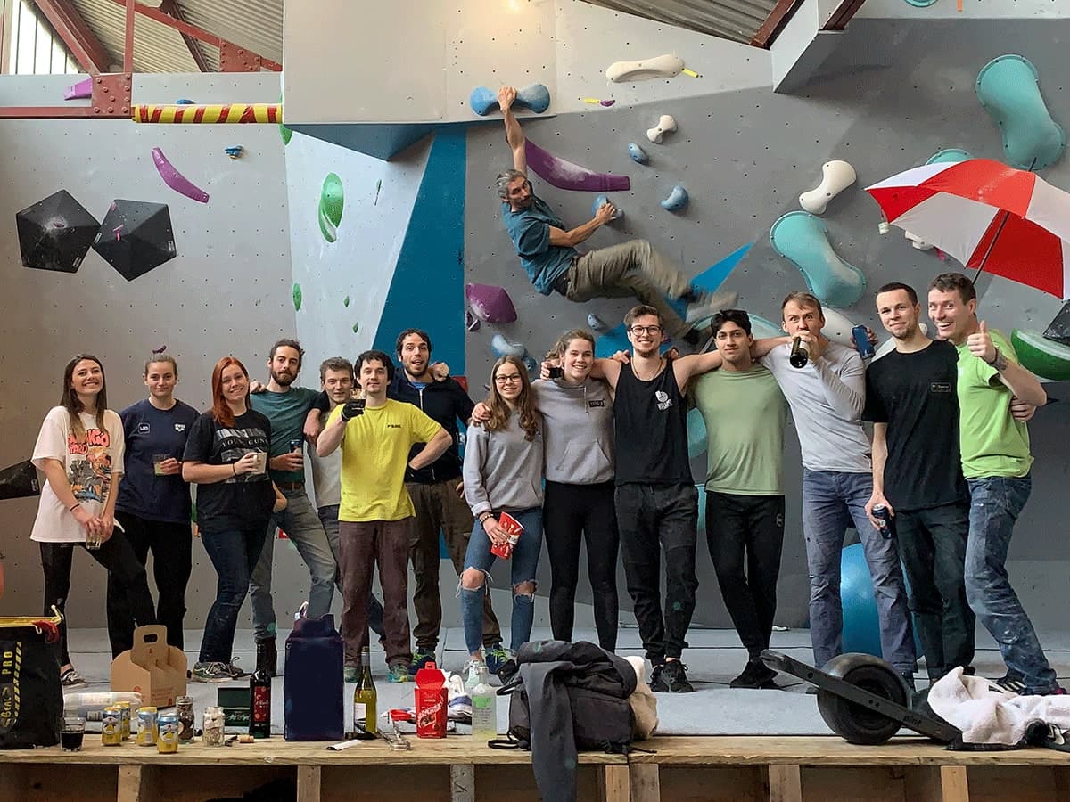 The Boulder Shack team lined up in front of the wall with drinks, one of them hanging off it above